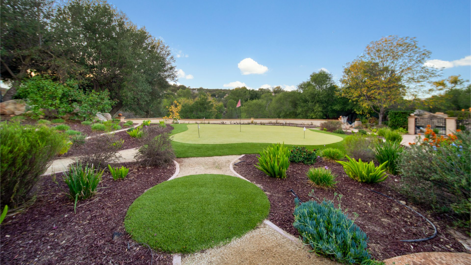 Landscaped garden with green lawn, purple flower beds, and a patio under a blue sky