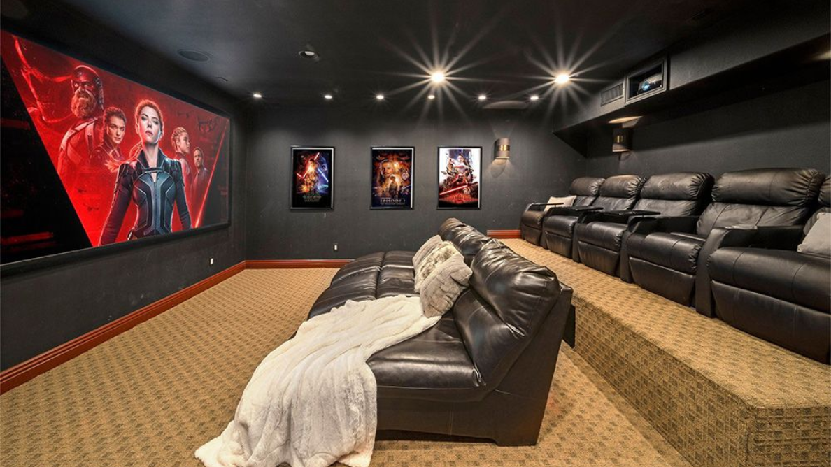 Home theater room with black recliners, red carpet, and a large movie screen.