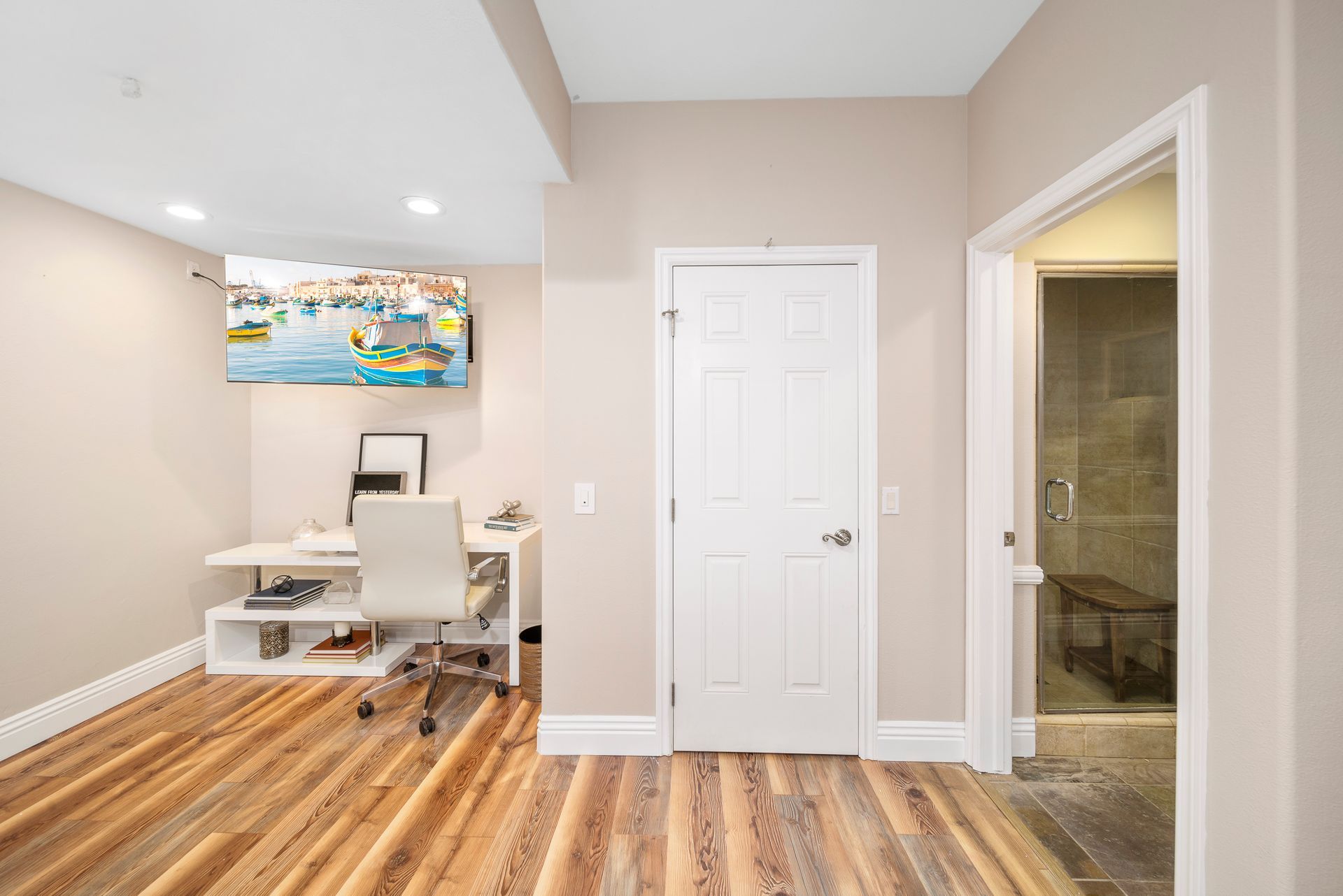 Bright home office with white desk and chair, hardwood floors, and a tiled bathroom doorway.