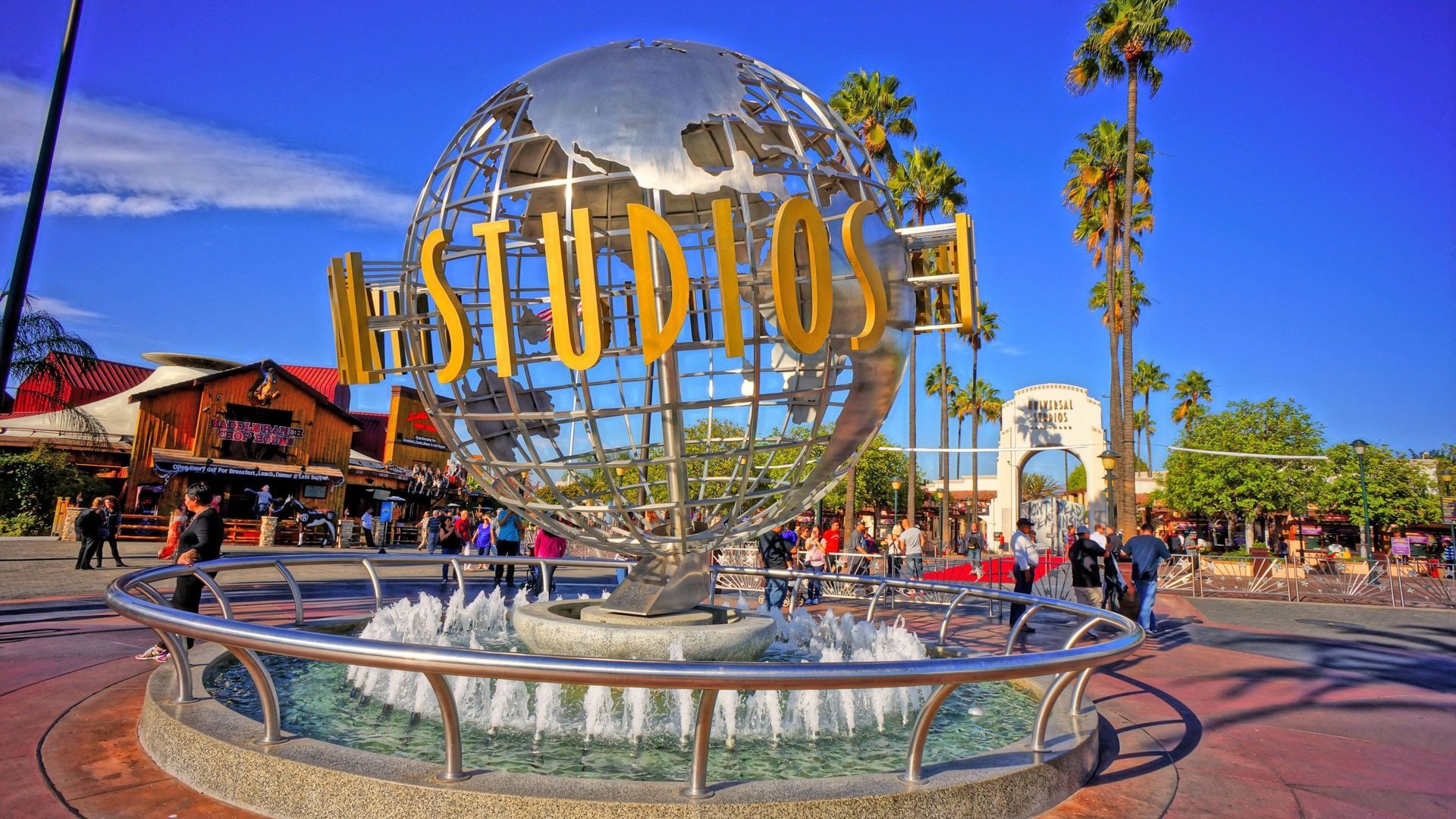 Universal Studios globe entrance with palm trees and visitors under a sunny blue sky