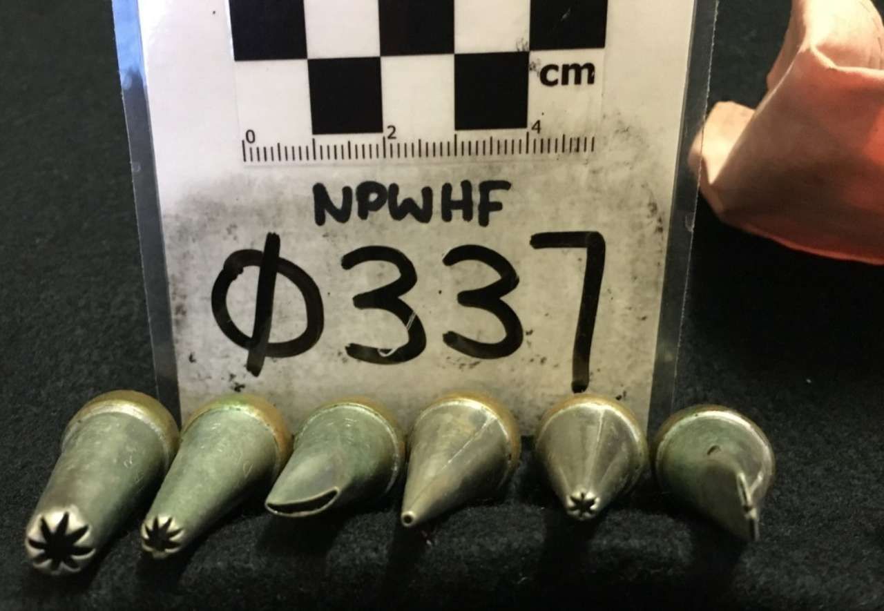 Five green artillery shells lined up in front of a white scale marked “Φ337” and “NPWHF.”