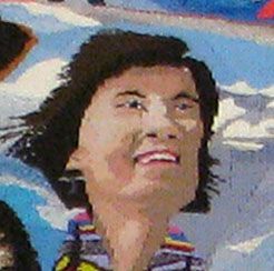 Person smiling with windblown hair against a blue sky and snowy mountains