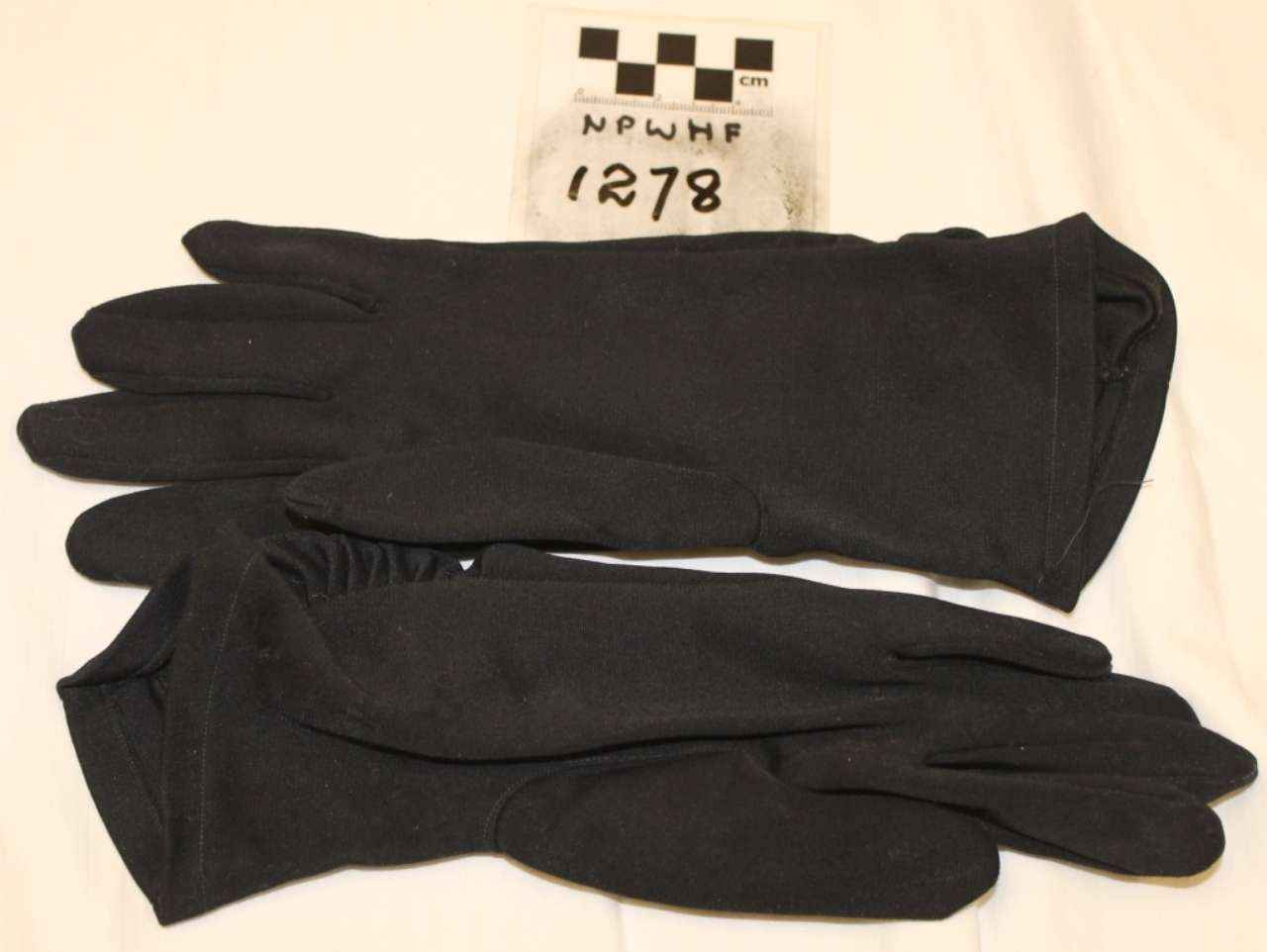 Black gloves stacked on a light surface beside a small numbered label.