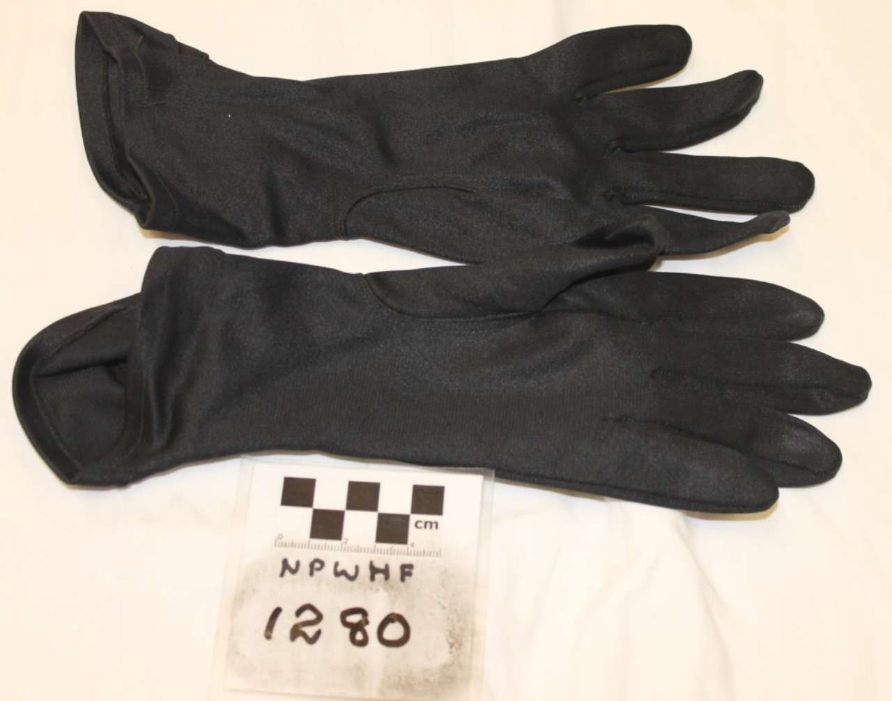 Two black gloves laid horizontally on a white background beside a small labeled tag.