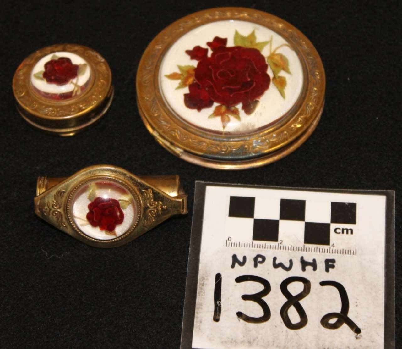 Three gold rings with red floral inlays beside a black-and-white measurement card labeled 1382