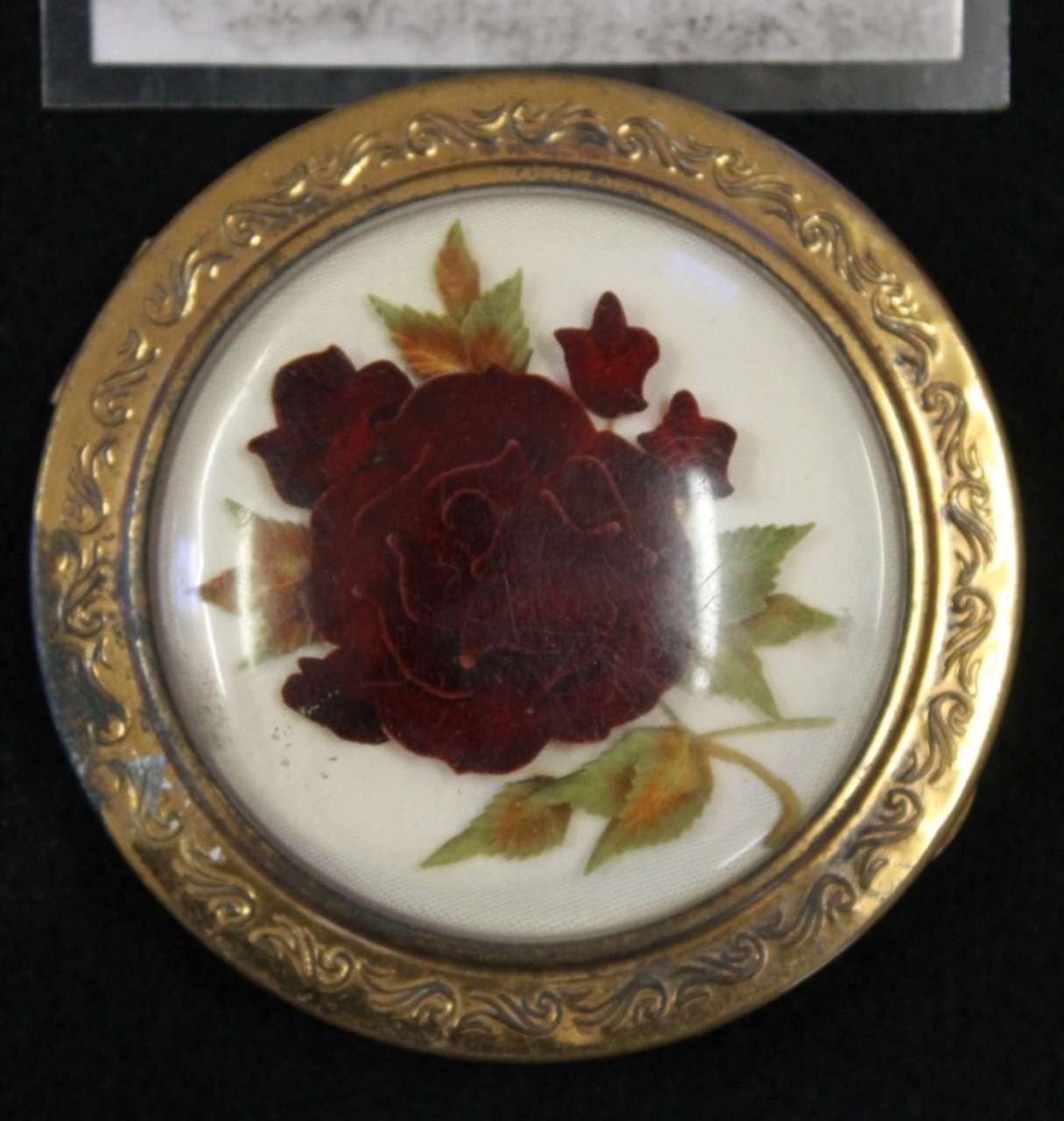 Round gold-framed floral plaque with a red rose design and green leaves on a white background