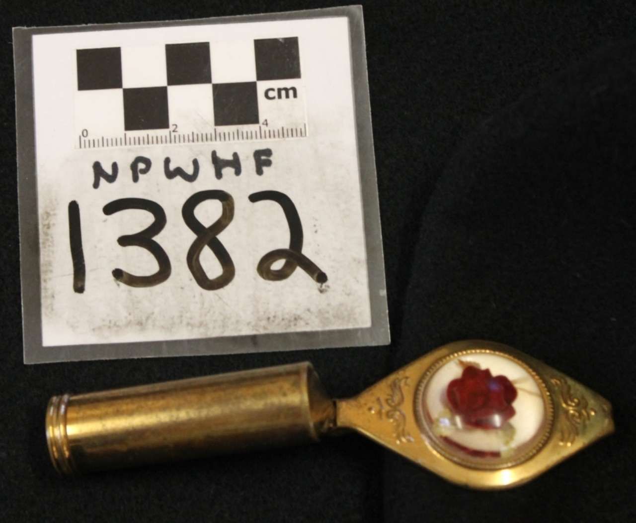 Brass-handled spoon with red wax seal beside a numbered scale card reading 1382