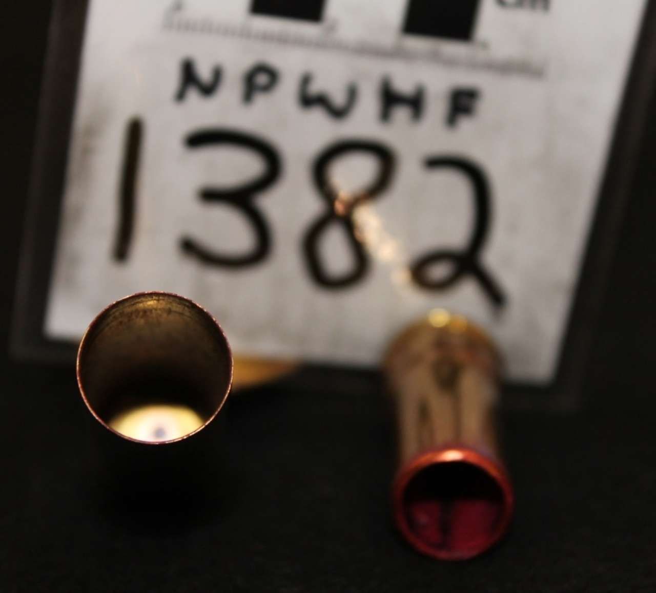 Close-up of two brass shell casings in front of a blurred white sign reading 1382.