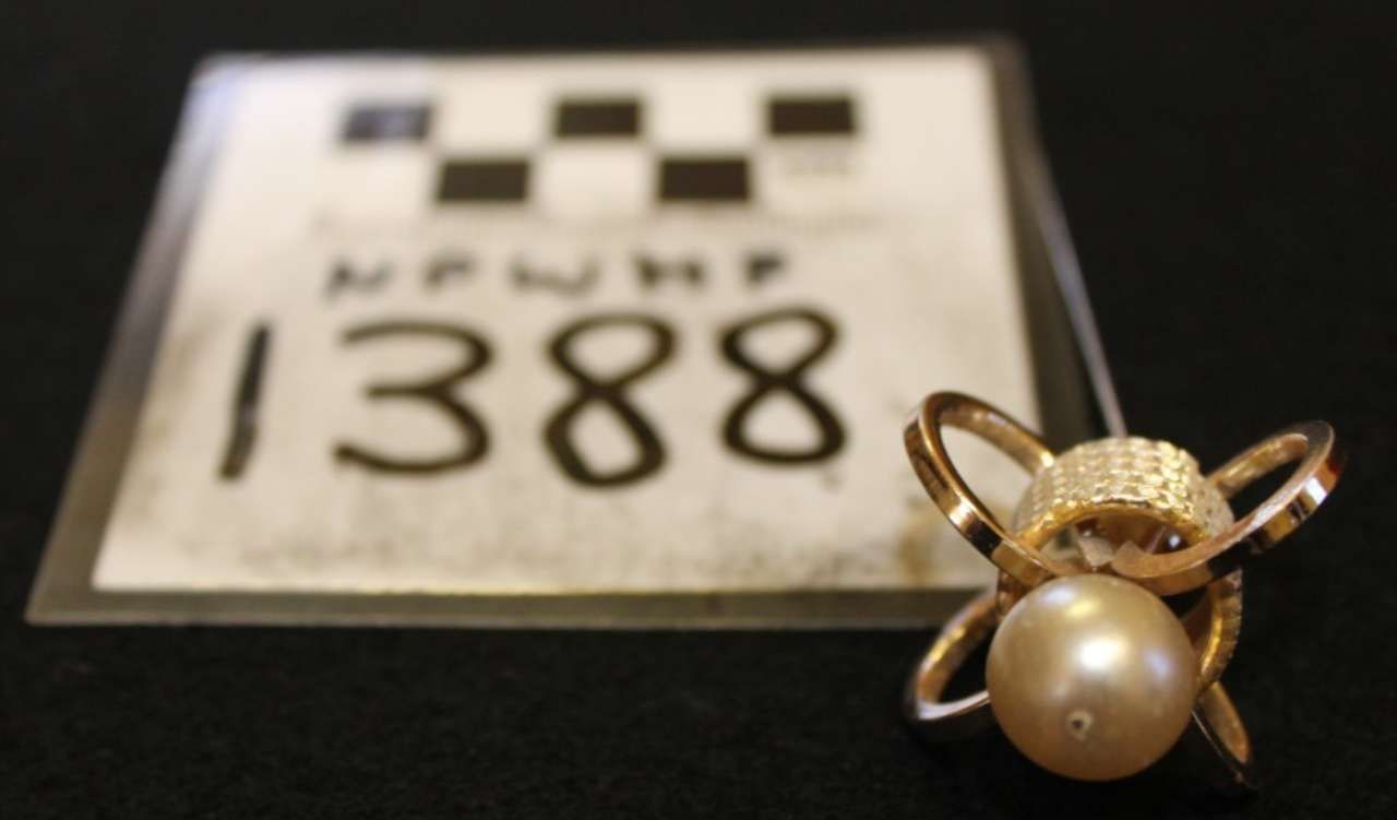 Evidence marker 1388 beside a gold ring with a pearl on a black surface