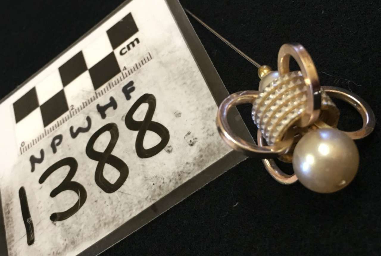 Close-up of a silver floral pendant necklace beside a black-and-white evidence tag labeled 1388.