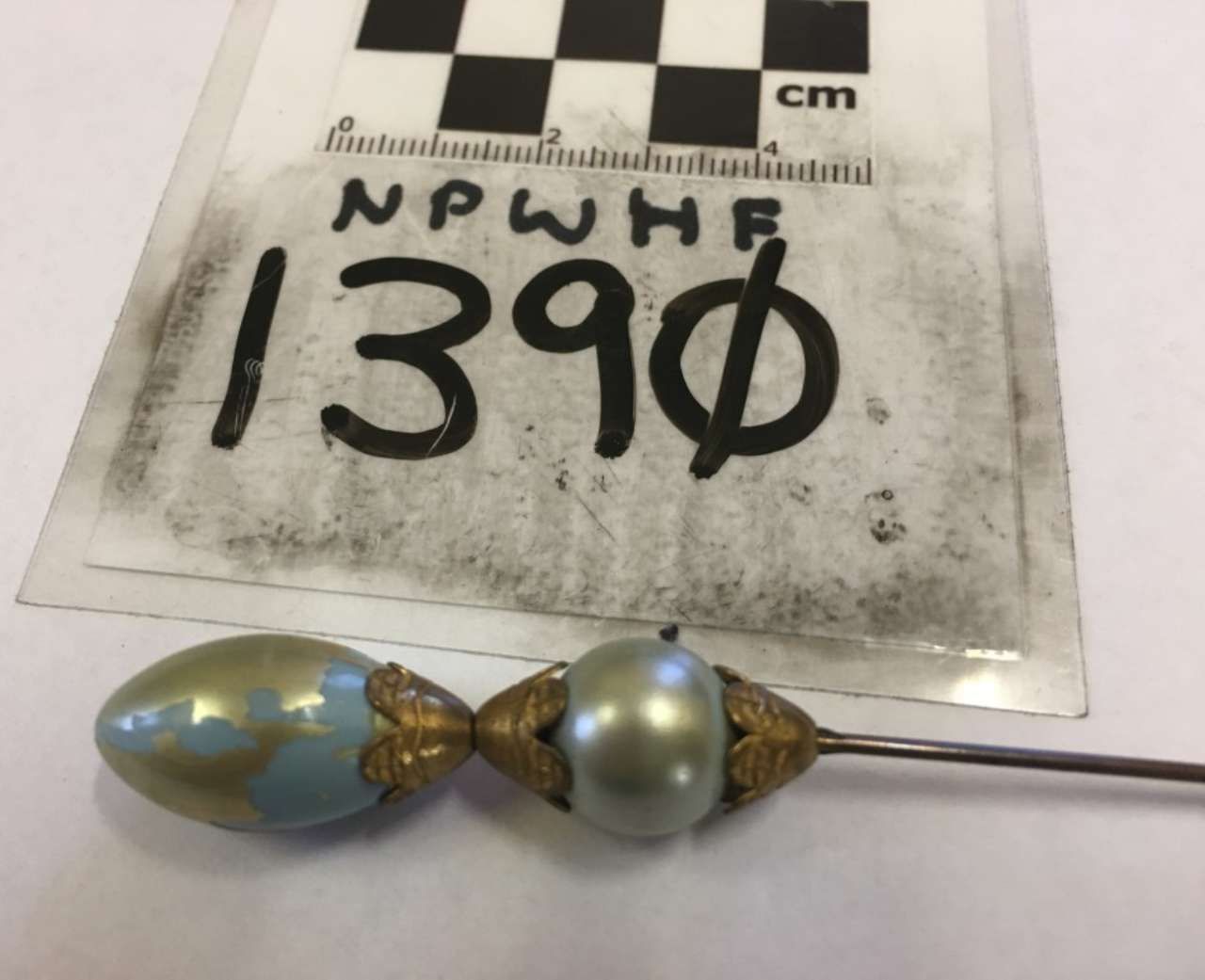 Small decorative bead-and-metal pin with blue and pearl beads on a measuring card labeled 1390.