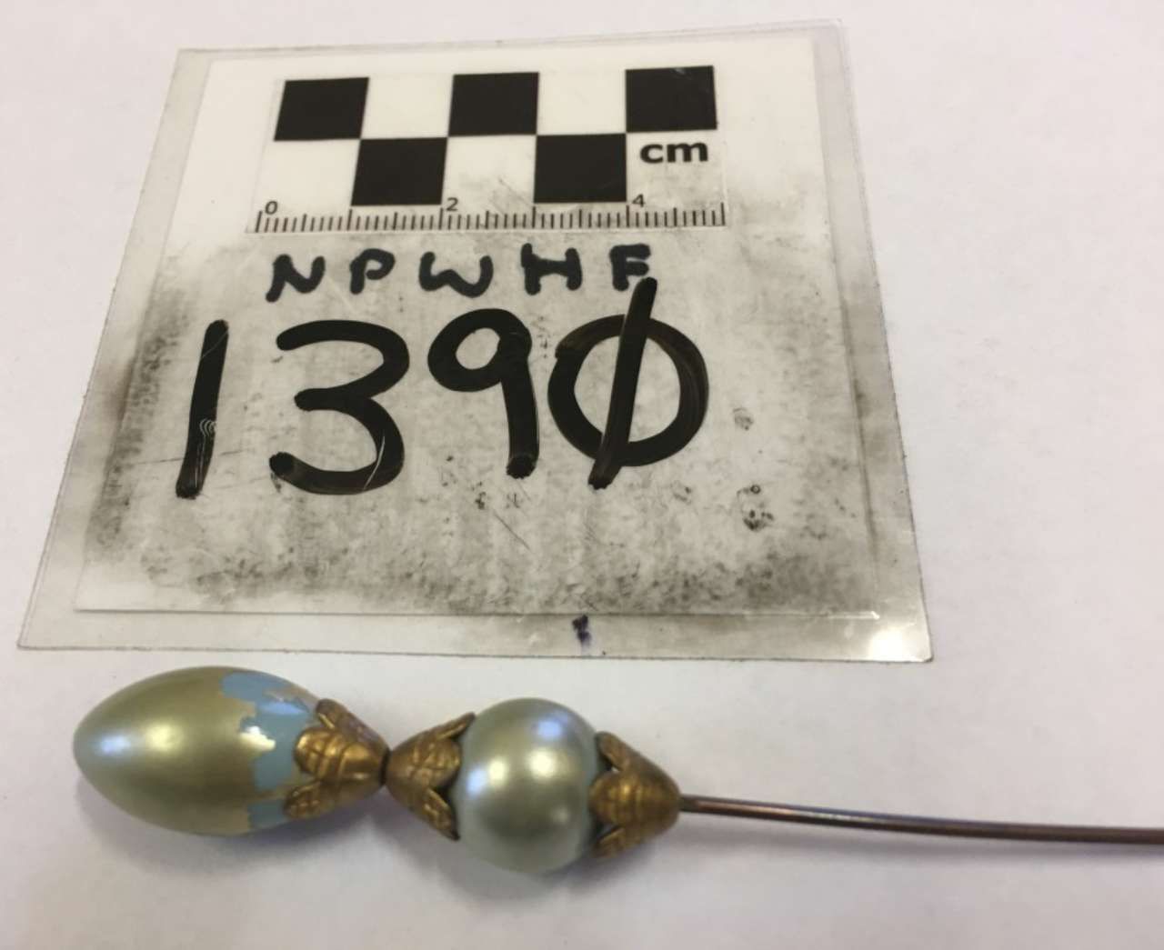 Two metallic beads on a wire beside a labeled evidence card with “1390” and a scale.