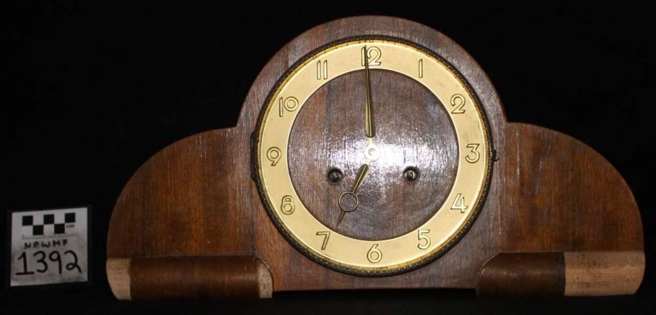 Wooden mantel clock with gold face and black numerals on a dark background