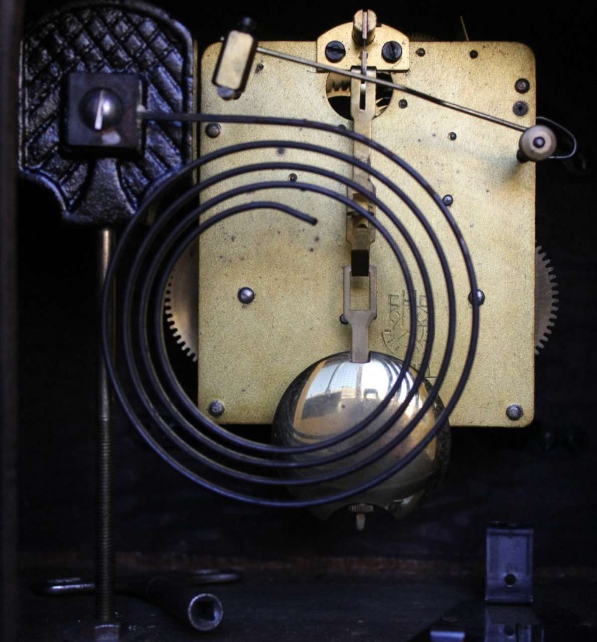 Close-up of a vintage clock mechanism with brass gears and a coiled black spring on a dark background