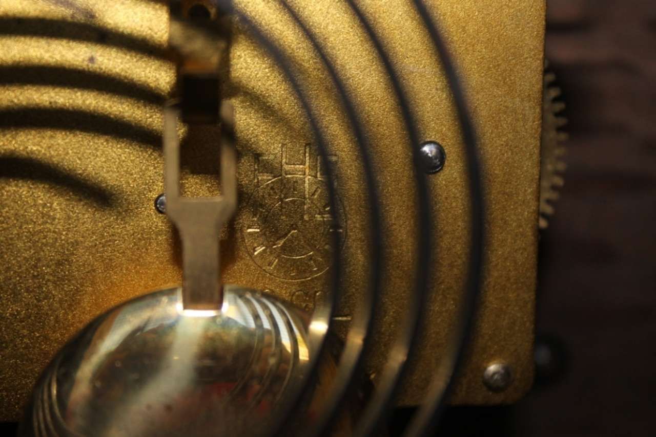 Close-up of a brass mechanical clock pendulum and gears in warm light