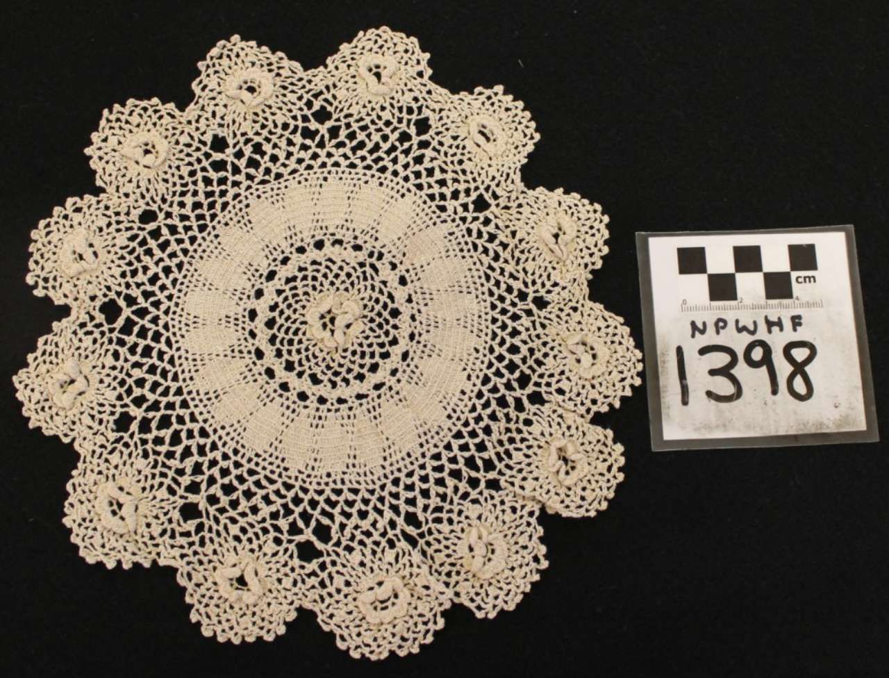 Beige crocheted lace doily on black background beside a numbered label