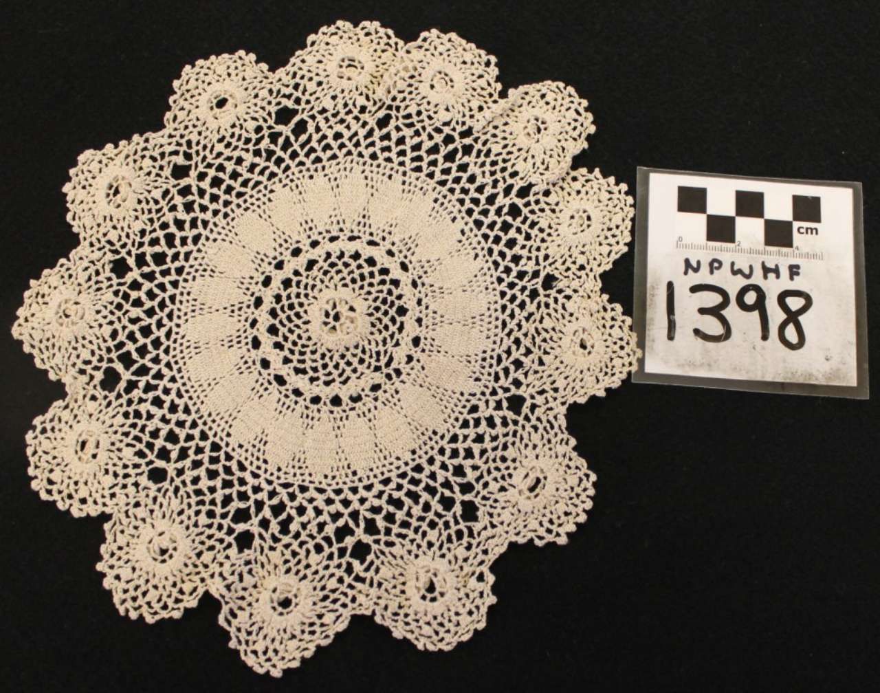 White crocheted lace doily beside a small labeled tag on a black background