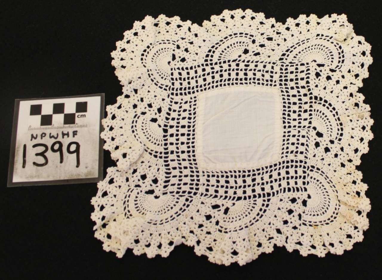 White crocheted lace doily with scalloped edges and square center beside a price tag reading 1399