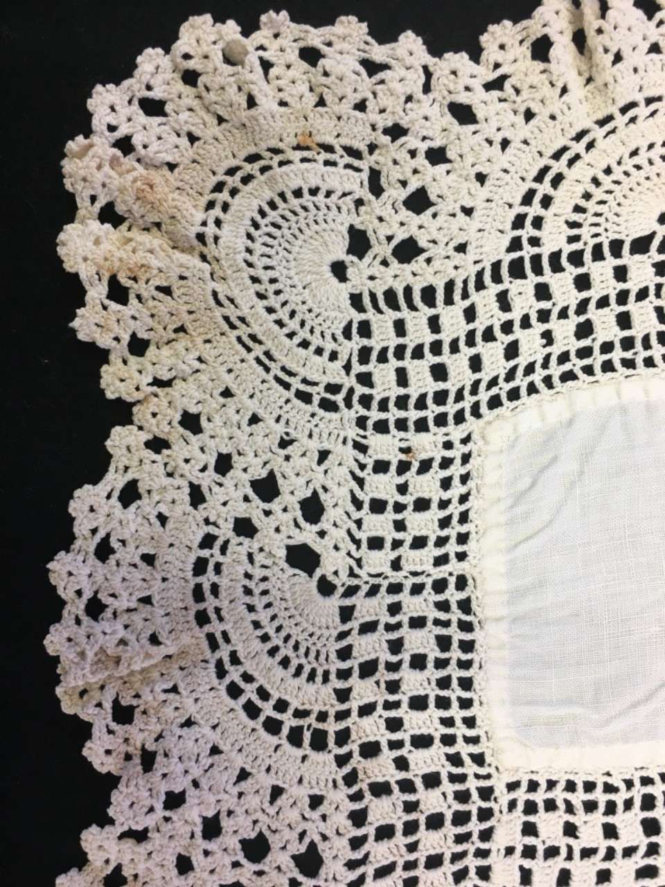 White crocheted lace doily with floral patterns and a square center on a dark background