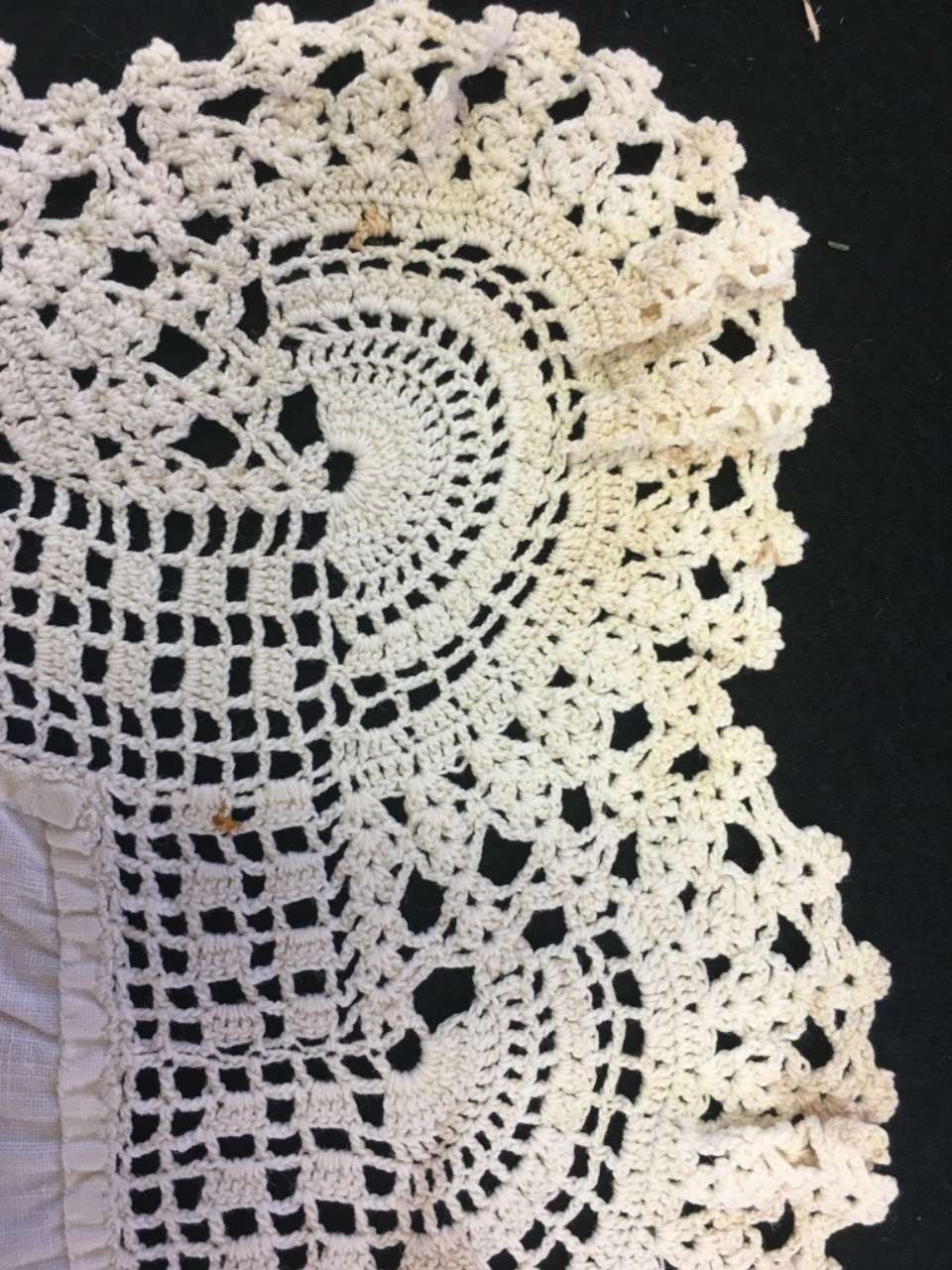 White crocheted lace doily with circular patterns on a dark background