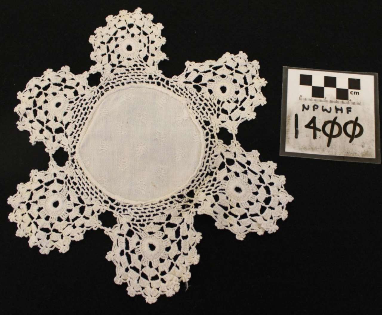 White crocheted lace doily with scalloped edges beside a small black-and-white label on a black background