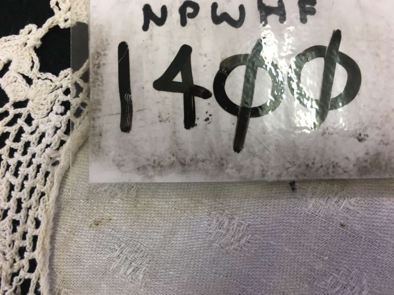 Handwritten sign reading “1400” on white paper, pinned above a gray fabric surface.