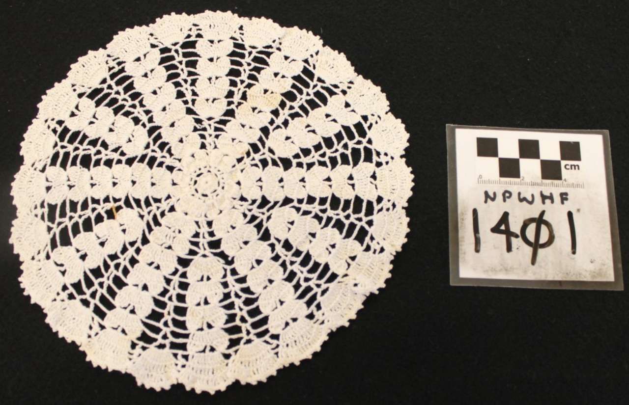 White crocheted doily beside a small labeled sign on a black background.