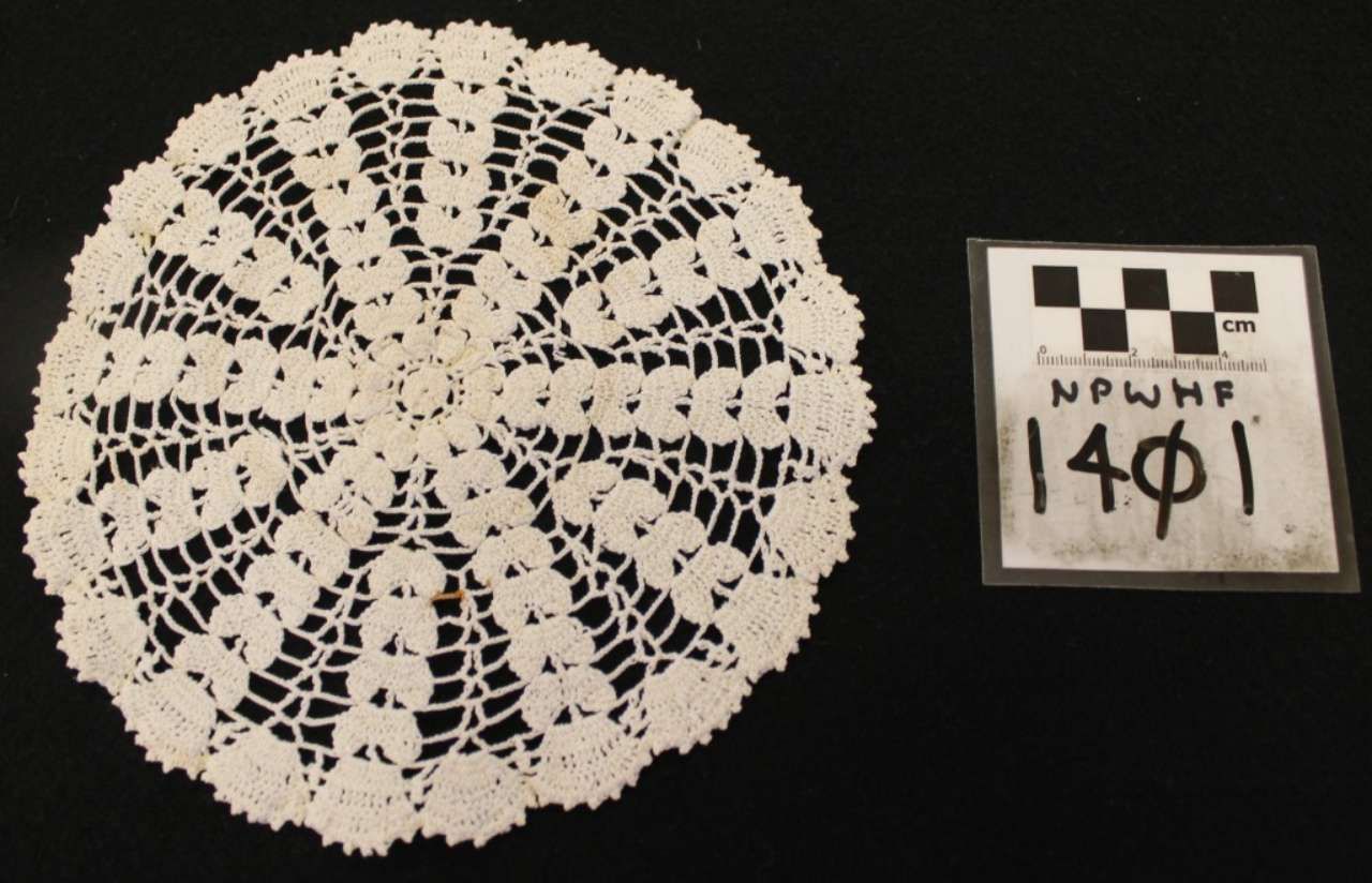 White crocheted doily beside a small label with handwritten text on a black background