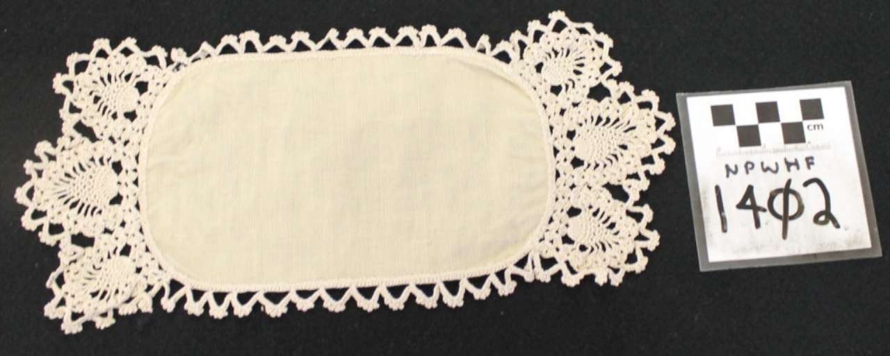 Cream lace doily with oval center beside a small numbered label on dark background