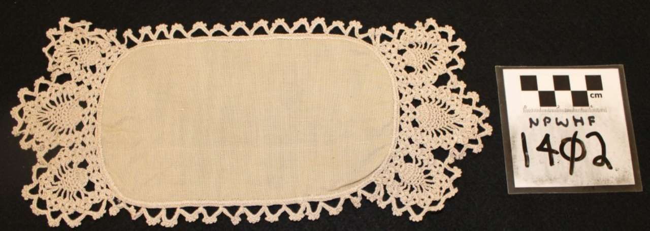 White lace doily beside a small black-and-white label with handwritten text on a beige background