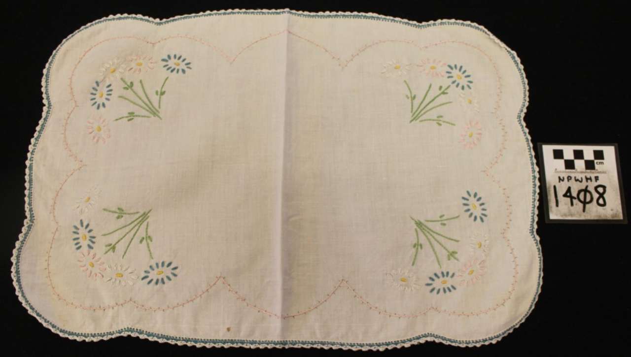 White embroidered linen doily with scalloped edges and small floral motifs on a black background