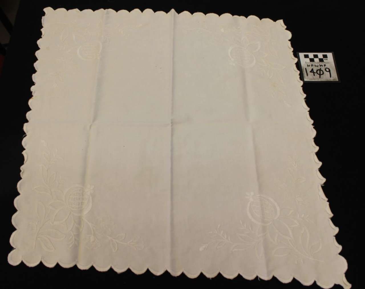 White scalloped paper doily with subtle embossed floral patterns on a dark background