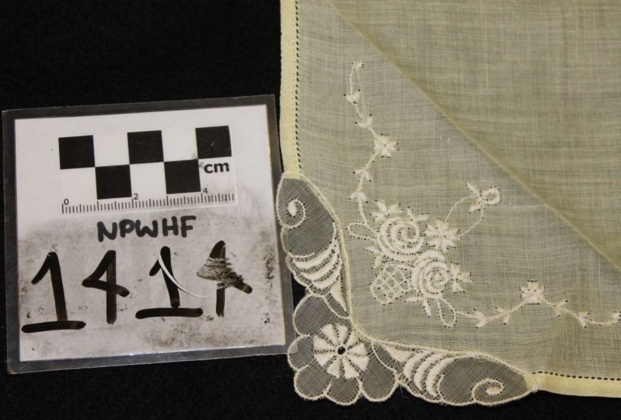 Beige lace fabric corner with floral embroidery beside a black-and-white measurement scale label