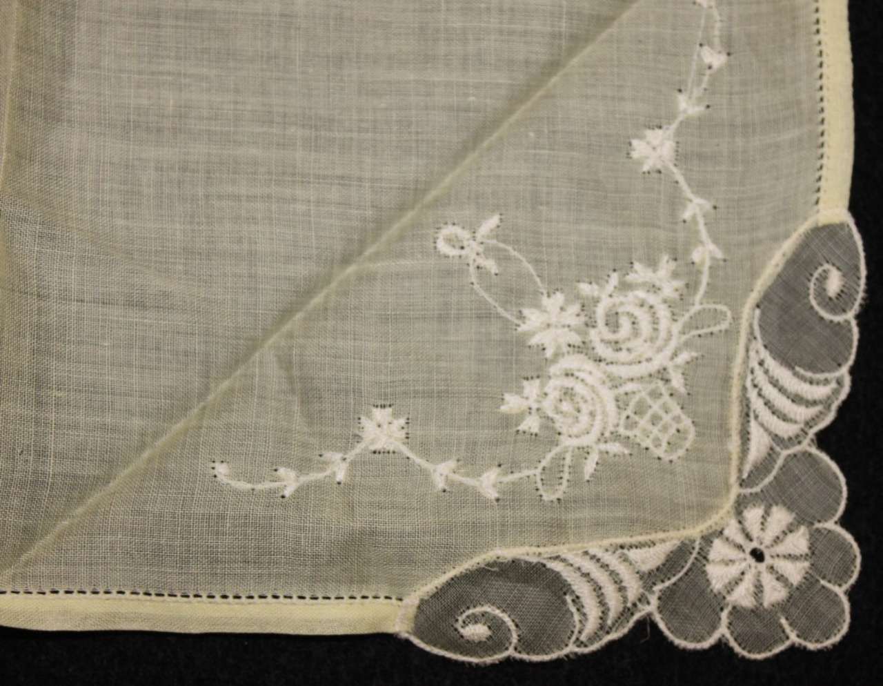 Sheer embroidered corner of a white lace handkerchief with floral and shell patterns