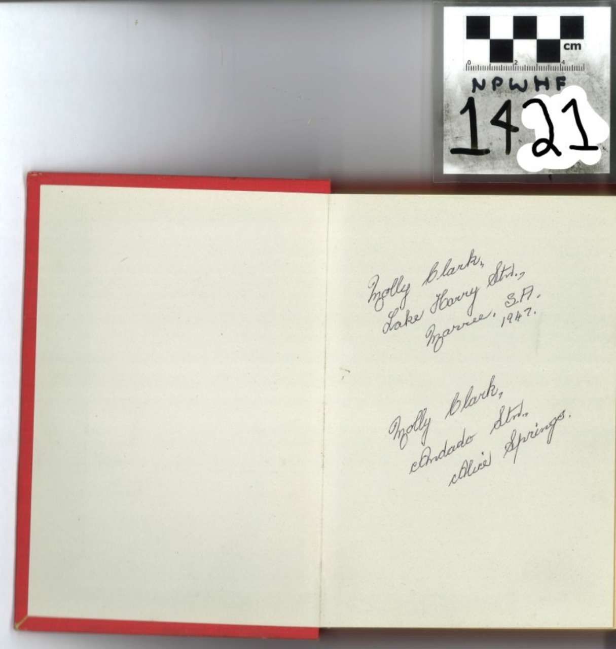 Open red-bound book with handwritten notes on cream pages, beside a small numbered label.