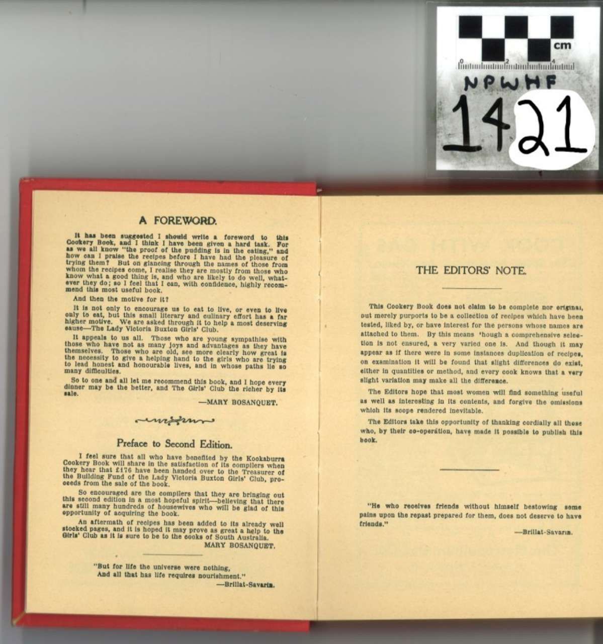 Open book with red cover edges and cream pages on a gray surface, beside a small numbered sign.