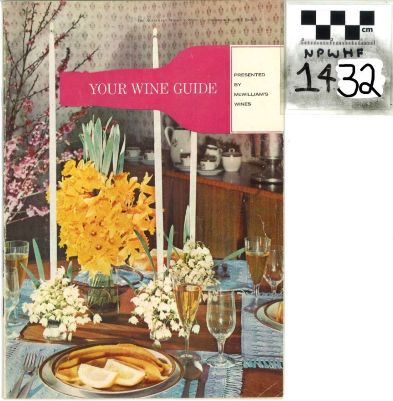 Wine guide cover on a dining table with flowers, wine glasses, and plates; small handwritten note at top right.