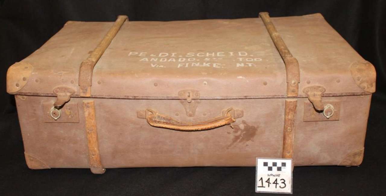 Weathered brown leather suitcase with straps and handle against a black background
