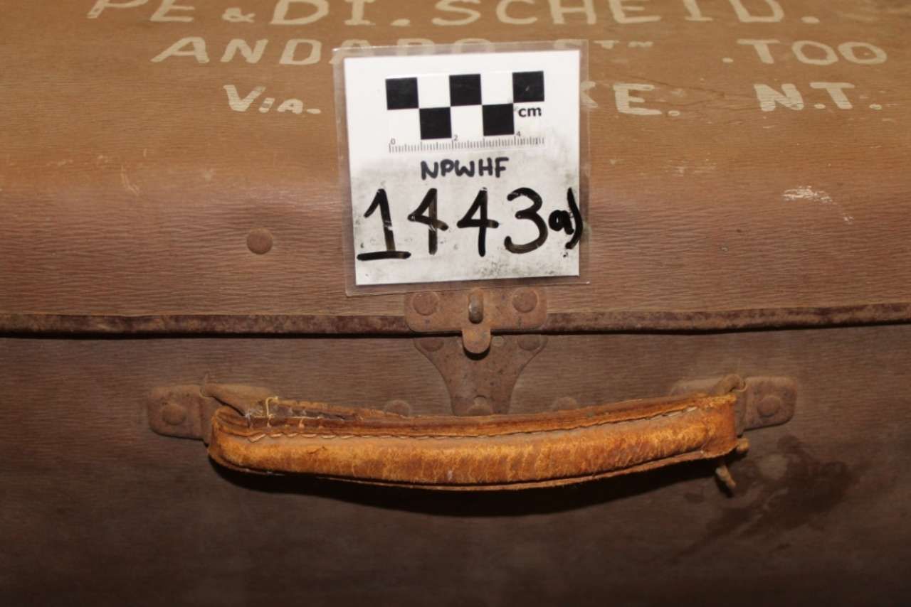Close-up of a worn wooden case with a numbered label and a metal handle.