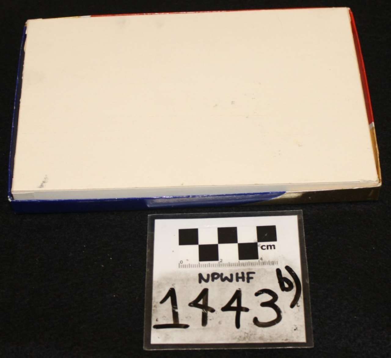 White rectangular box with red and blue edges next to a small labeled scale card on a black background
