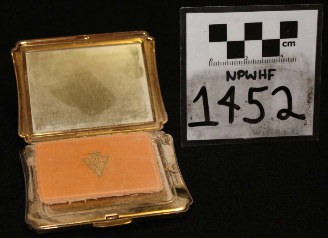 Open gold compact with tan powder beside a labeled evidence card marked 1452.