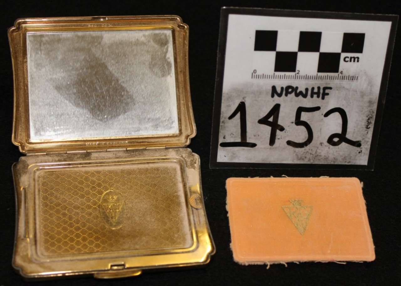 Open gold compact, orange insert, and label card marked 1452 with scale ruler