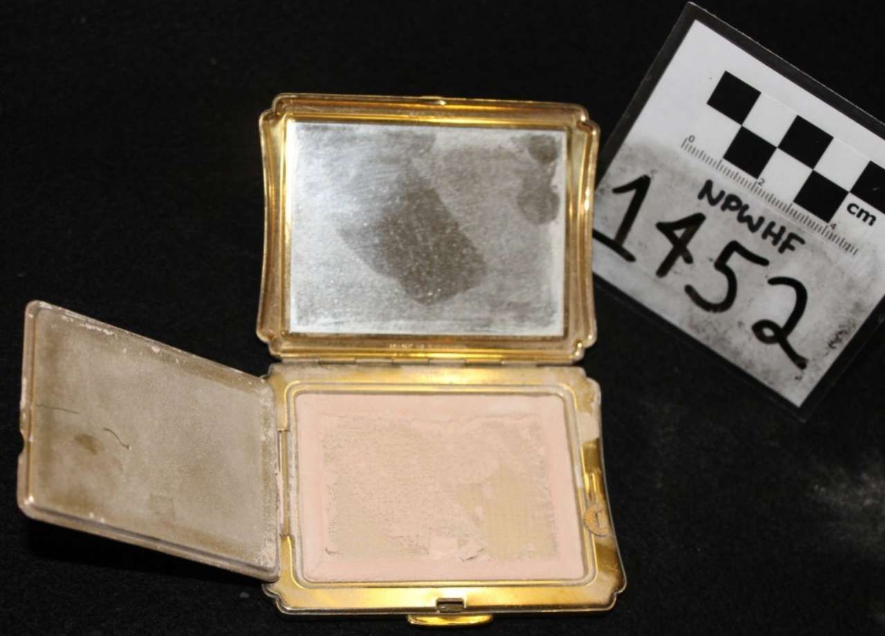 Open gold compact with mirror, powder, and sponge, beside a numbered evidence tag.