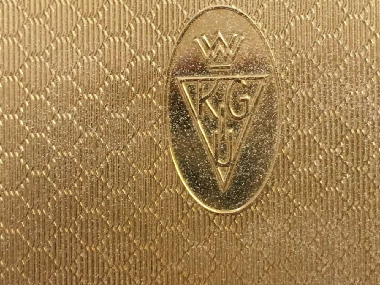 Gold-colored textured fabric with an oval WGC monogram emblem centered.