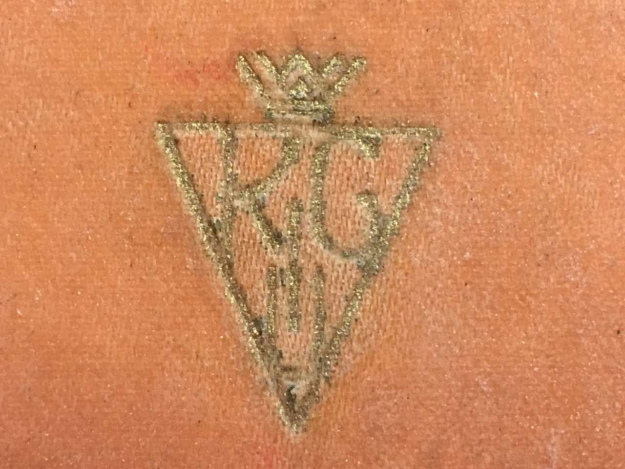 Small faded triangular tattoo with a crown-like top on skin, in black and green ink