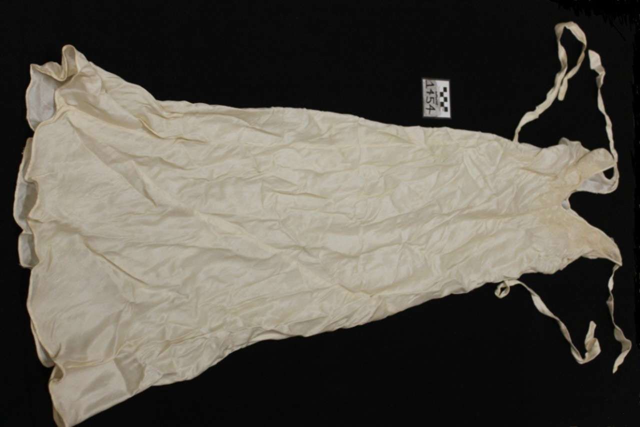 White crumpled drawstring garment bag laid flat on a black background.