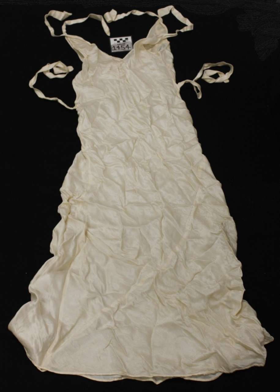 White crinkled dress with tied shoulder straps laid flat on a dark background
