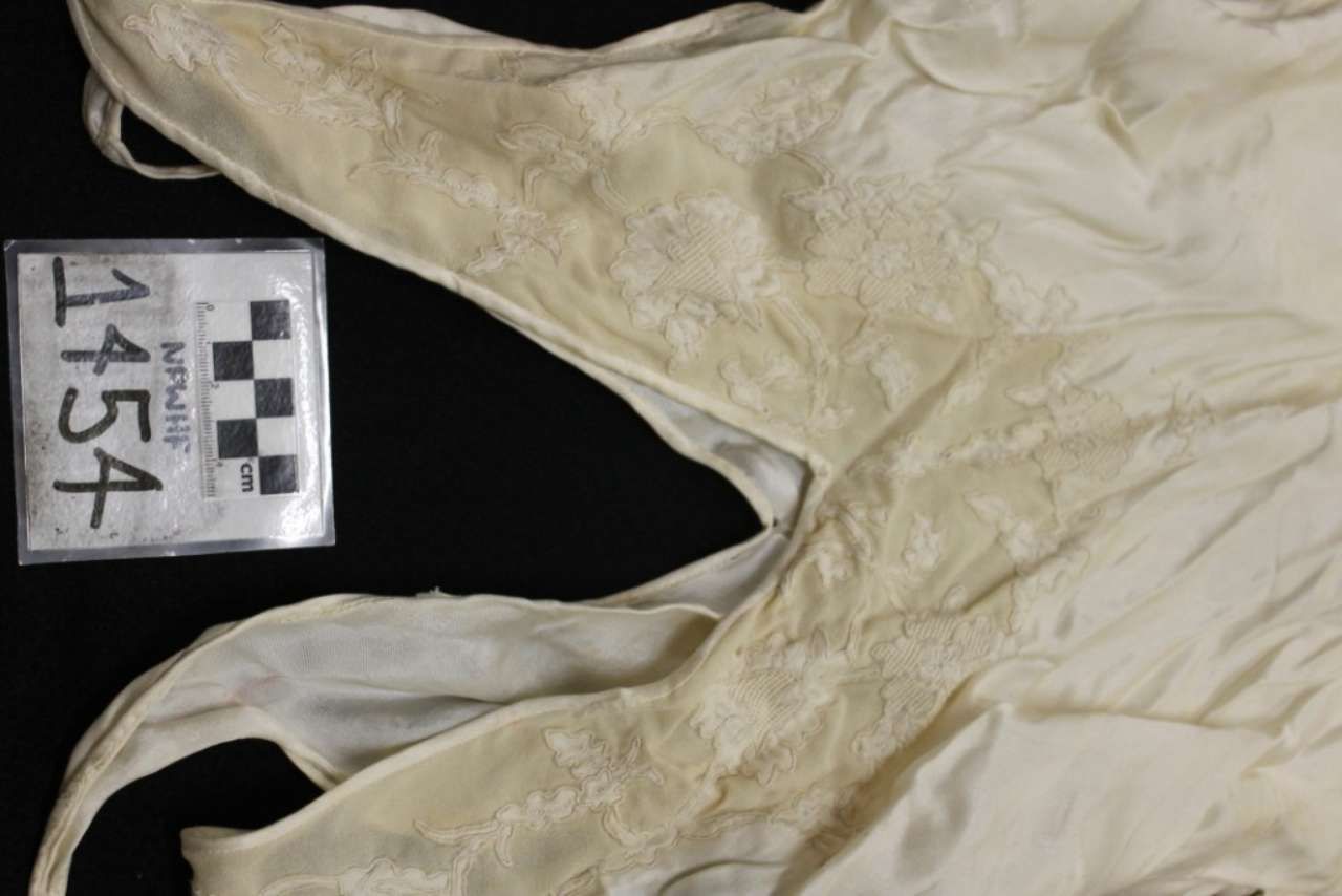 Beige wrinkled garment on a black background with a numbered museum tag