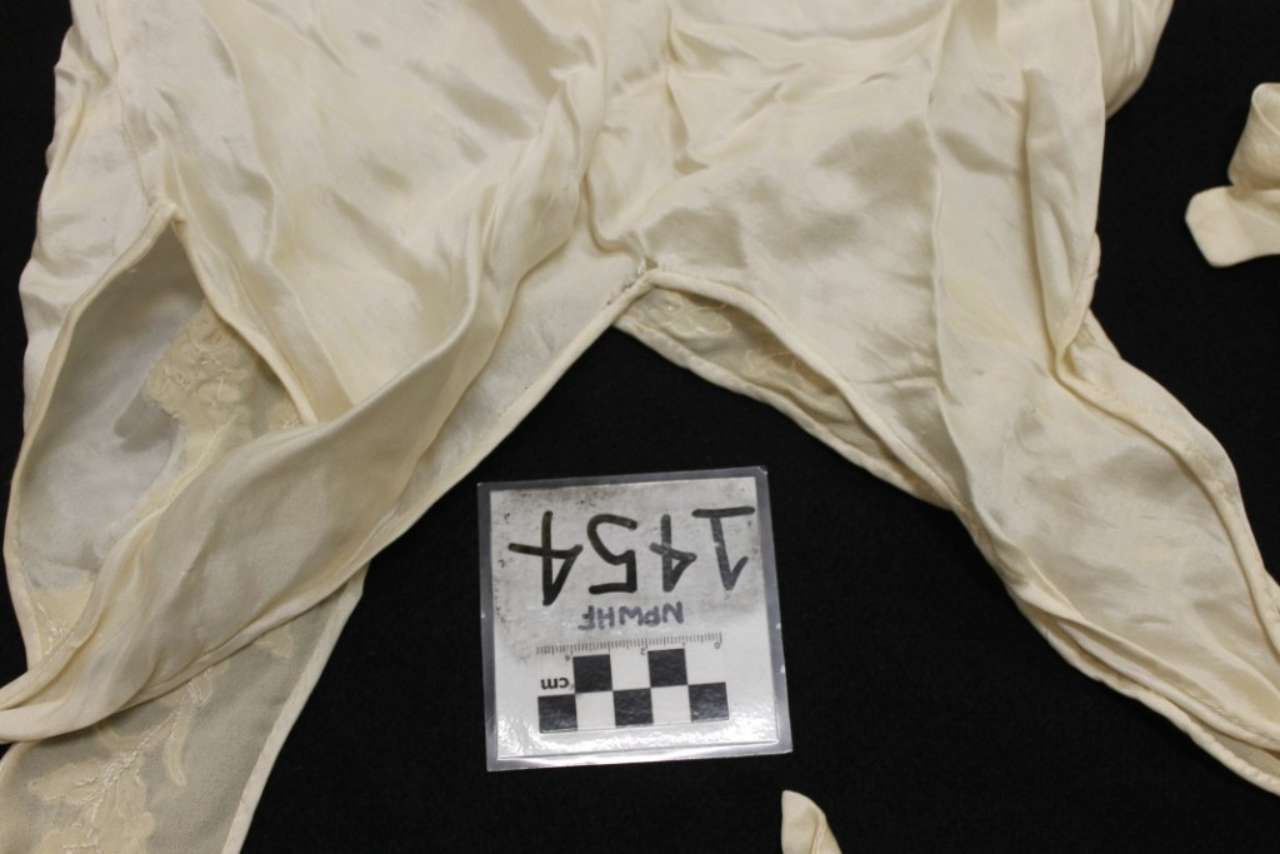 White pants laid flat on a dark background with a small numbered evidence card.