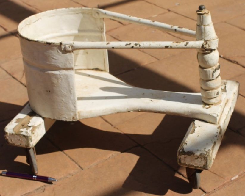 Old white metal chair frame with four legs on a sunlit tiled floor